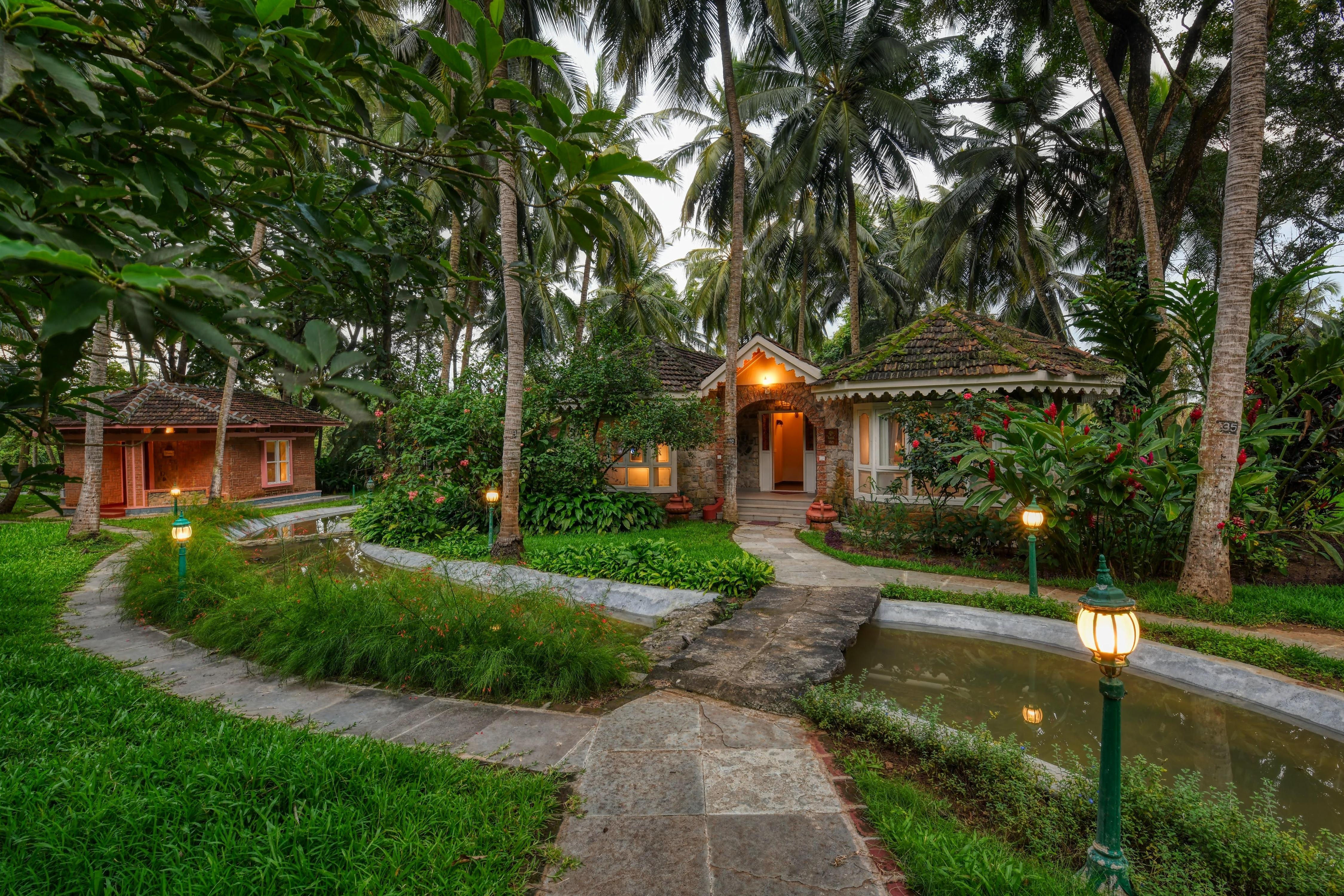 Traditional cottages surrounded by lush greenery and palm trees at Kairali—The Ayurvedic Healing Village in Palakkad, offering a peaceful and immersive Ayurvedic retreat.